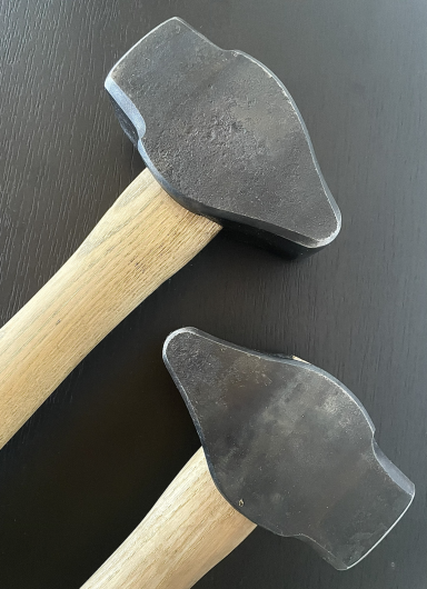 Zwei geschmiedete Hämmer mit Holzgriffen auf einem dunklen Untergrund.
