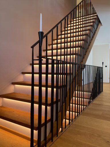 Moderne Treppe mit Holzstufen, beleuchtet und geschmiedetem Geländer mit freier Stabaufteilung.