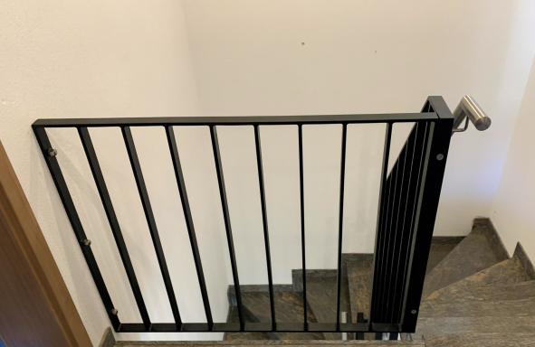 Schwarzes Treppenschutzgitter an einer Wand vor einer Treppe.