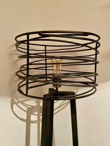 Schwarze Metalllampe mit spiralförmigem Korb und sichtbarem Glühbirnenelement.