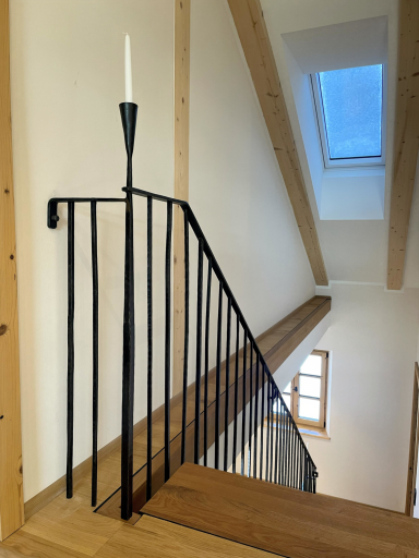 Schwarzes Geländer mit Kerzenhalter und Holztreppe in einem Raum mit Dachfenster.